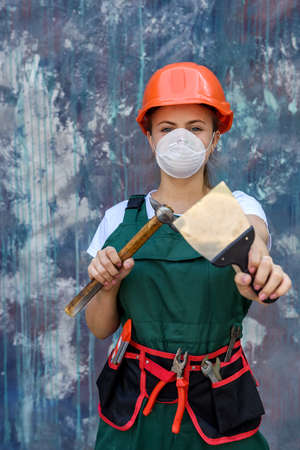 Renovation and remodeling concept. Woman in helmet and protective mask posing with hammer and spatulaの写真素材