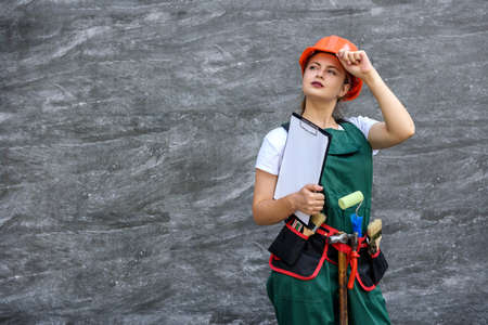 Woman in protective uniform and helmet posing with clipboard and tool beltの写真素材