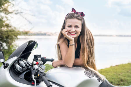 Beautiful young woman posing with motorcycle outside