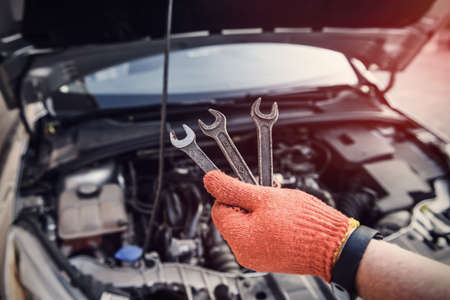 Male hand in glove holding spanners against car engineの写真素材