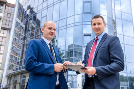 Two serious businessman posing against business centerの写真素材