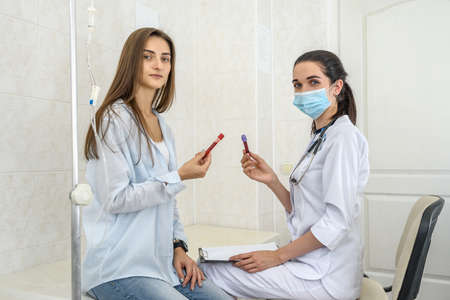 Patient with test tube with blood posing in hospital. Doctor with clipboard and patient sitting on sofaの写真素材