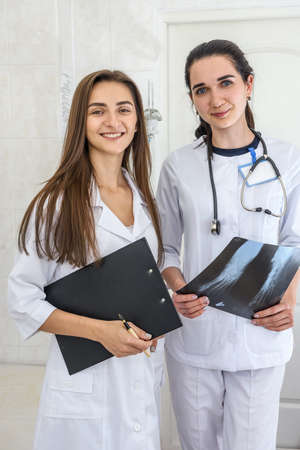 Two young doctors discussing patient's foot x-ray. One doctor holding film opposite herself and other holding clipboardの写真素材