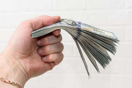Hand with dollars pile close up on wall brick background