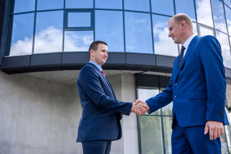Business partners handshaking before big building outdoors