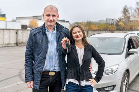 Smiling couple posing near new car with keys