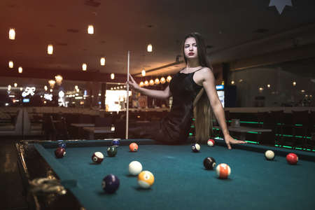 Beautiful woman in black dress posing with billiard cue