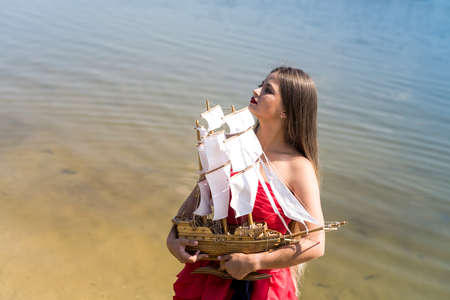 Woman in red dress holding boat model on the beachの写真素材