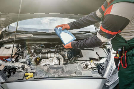 Male hands with oil bottle above car engine