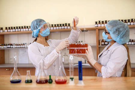 Chemists working in laboratory. Young women in protective uniforms with test tubes making experimentsの写真素材
