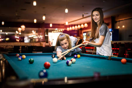 Beautiful woman with her friend playing billiard in pubの写真素材