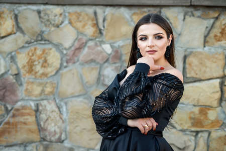 Fashion smiling woman in black dress on a brick background. Fashion