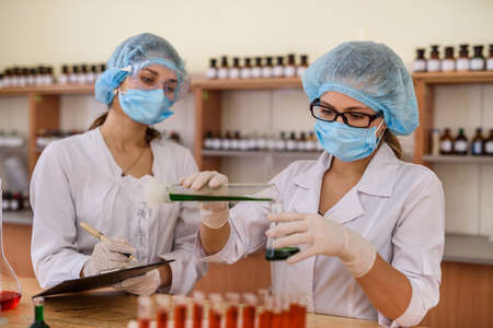 Chemists working in laboratory. Young women in protective uniforms with test tubes making experimentsの写真素材