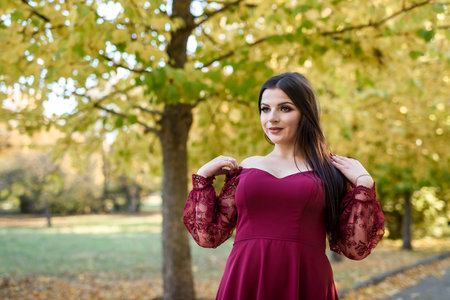 Young princess  in a beautiful red dress in park. The background is bright, golden autumn nature.の写真素材