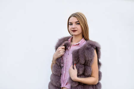 Beautiful young woman in fur coat on white wall. Beauty and fashion.の写真素材