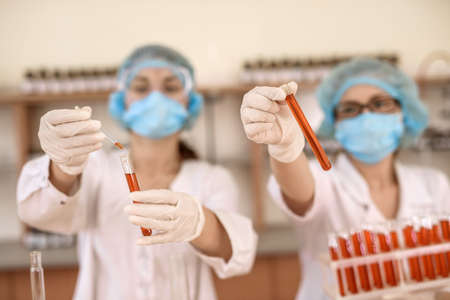 Chemists working in laboratory. Young women in protective uniforms with test tubes making...