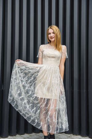 Young woman in evening dress posing on city street, dark wall backgroundの写真素材