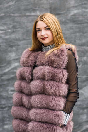 Portrait of fashion woman. Beautiful woman in fur coat posing on dark wall backgroundの写真素材