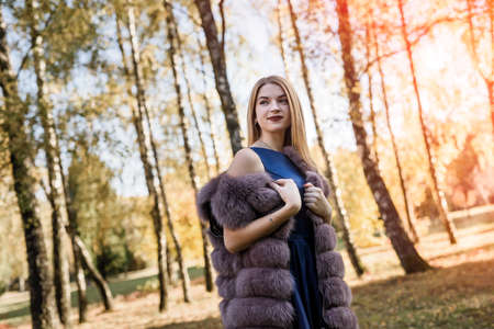 Fashion dresses woman in fur coat and dress posing in autumn parkの写真素材