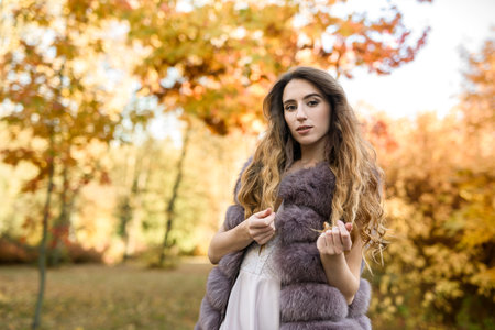 Fashion dresses woman in fur coat and dress posing in autumn parkの写真素材