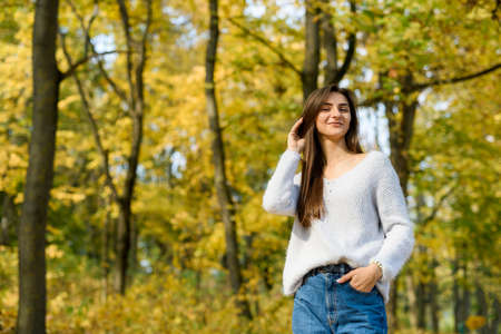 Autumn landscape. Woman in casual wear posing in park with yellow leaves