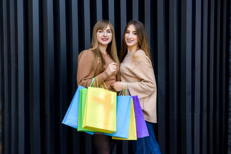 Happy women with shopping bags in fur coats posing on city streetの写真素材