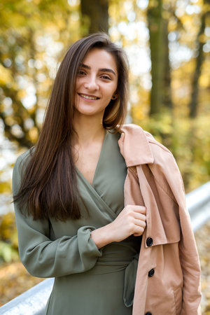 Portrait of brunette woman in green dress posing in autumn parkの写真素材