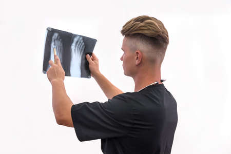 Doctor examining patient's x-ray. Young man in blue uniform holding foot x-ray and looking on itの写真素材
