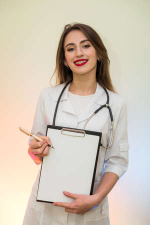 Doctor holding clipboard with pen. Pretty woman in medical form smilingの写真素材