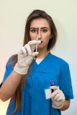Doctor with syringe and red test tube posing in hospitalの写真素材