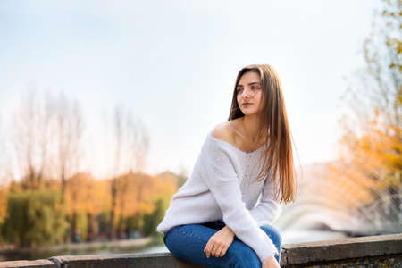Portrait of young woman in casual wear posing near fountain outdoors. Autumn in cityの写真素材