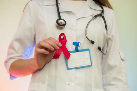 Female doctor in medical uniform holding red ribbon. AIDS day concept