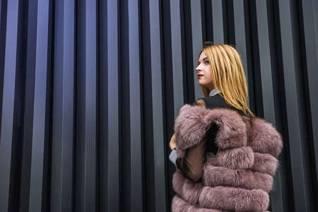 Portrait of fashion woman. Beautiful woman in fur coat posing on dark wall backgroundの写真素材
