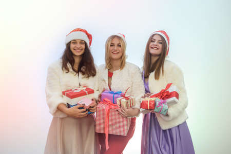 Beautiful ladies with gift boxes in fashion evening dresses and santa hats