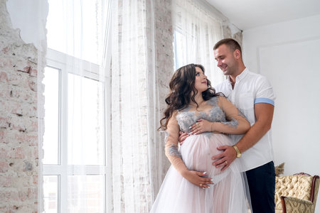 In expecting. Happy pregnant pair in fashion clothes posing in studioの写真素材