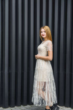 Young woman in evening dress posing on city street, dark wall backgroundの写真素材