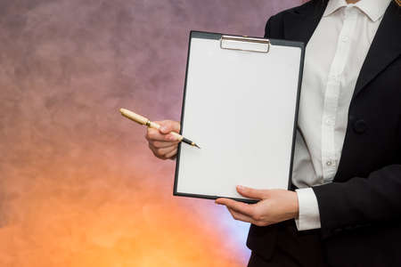 Beautiful business lady pointing with pen on clipboard proposing sign a contractの写真素材