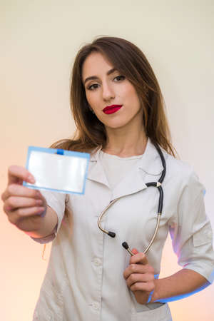 Cheerful and attractive doctor in medical uniform posing with stethoscope and badge in hospitalの写真素材