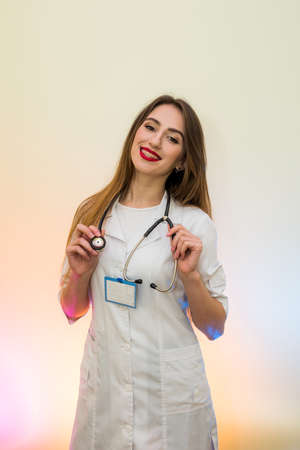 Cheerful and attractive doctor in medical uniform posing with stethoscope and badge in hospitalの写真素材