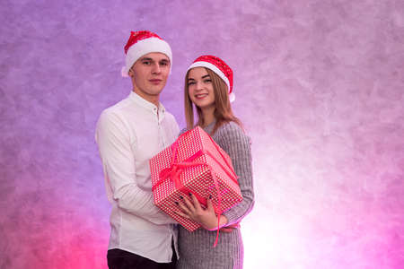 Beautiful couple with present box posing in santa hats in studio
