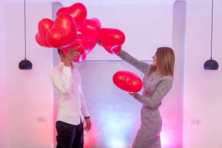 Beautiful couple with red air balloons celebrating Valentine's Day posing in studio