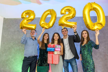 Cheerful company of friends with golden air balloons and present box celebrating New Year