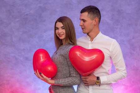 Happy couple in love posing with red air balloons in shape of heart