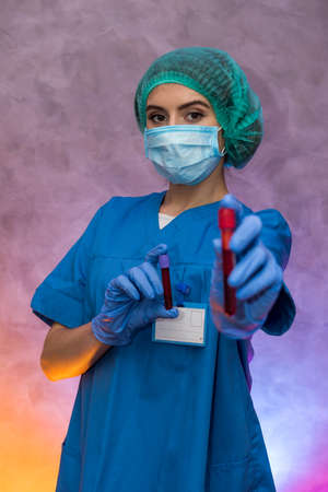 Medical worker with test tubes with blood pose in laboratory. Beautiful woman in protective uniform