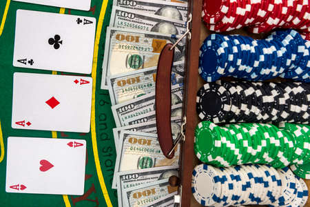 Poker chips in the case on a gaming table with cards and dollars.