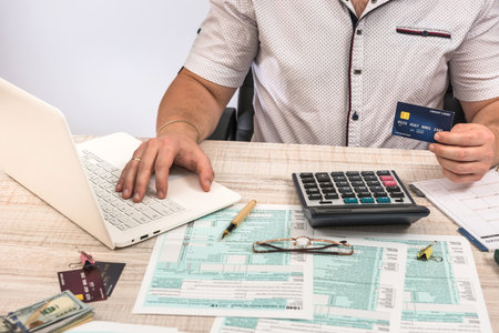 Man filling 1040 tax form at workplace. Performing tax calculations. Close up