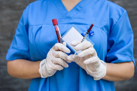 Doctor with test tube and syringe with red medicament. She's in blue uniform with protective mask on...