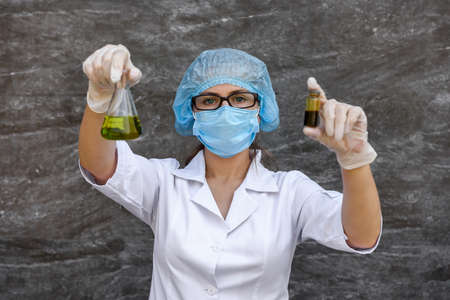 Chemist examining test tube with substance. She's in protective uniform over gray abstract gray backgroundの写真素材