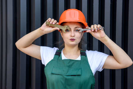 Beautiful woman in helmet and coverall holding fixing key over eyeの写真素材