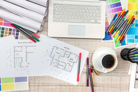 Close up view of color palette swatch and house building plans on office desk with laptop and cup of...